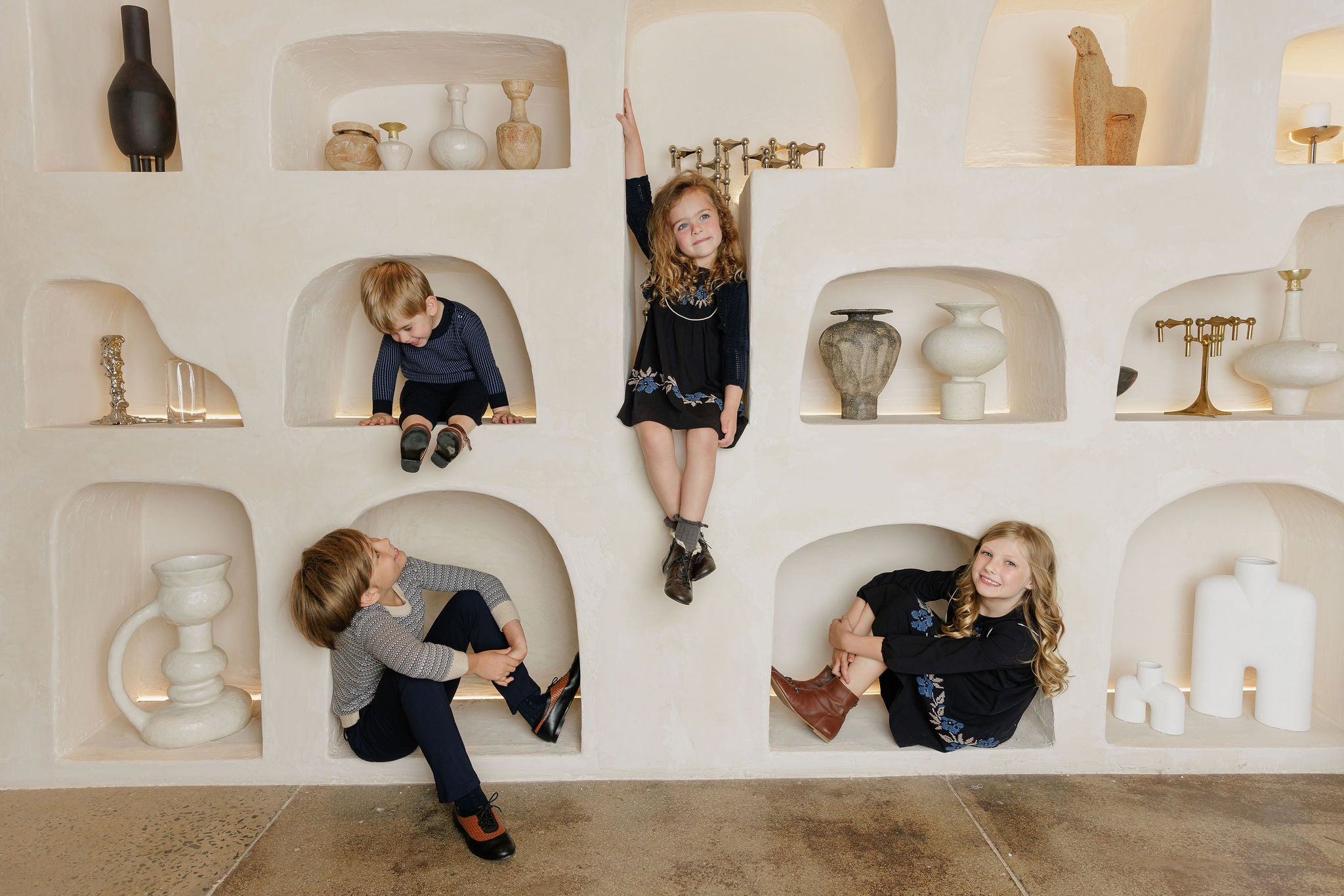 Four children playing in a decorative wall dressed in Looms Knits Winter Collection.